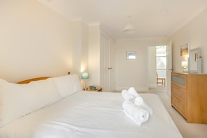 A hotel room with a large bed, a bedside table with a lamp, a wooden dresser, and a door leading to another room. - 2 Bed in Sidmouth (oc-t32948) (Sidmouth)