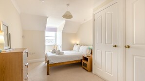 A bedroom with a bed, bedside tables, a dresser, a window, and a door. - 2 Bed in Sidmouth (oc-t32948) (Sidmouth)
