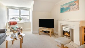 A living room with a fireplace, a television, and a window with a view of buildings. - 2 Bed in Sidmouth (oc-t32948) (Sidmouth)