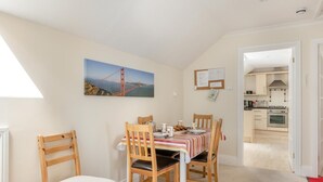 A dining area with a table set for four, a kitchen visible through an open door, and a painting of a bridge on the wall. - 2 Bed in Sidmouth (oc-t32948) (Sidmouth)