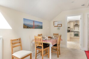 A dining area with a table set for four, a kitchen visible through an open door, and a painting of a bridge on the wall. - 2 Bed in Sidmouth (oc-t32948) (Sidmouth)