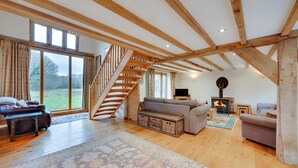 A spacious living room with a wooden staircase, a fireplace, and a large window overlooking a garden. - 2 Bed in Guestling (oc-rh1142) (Westfield)