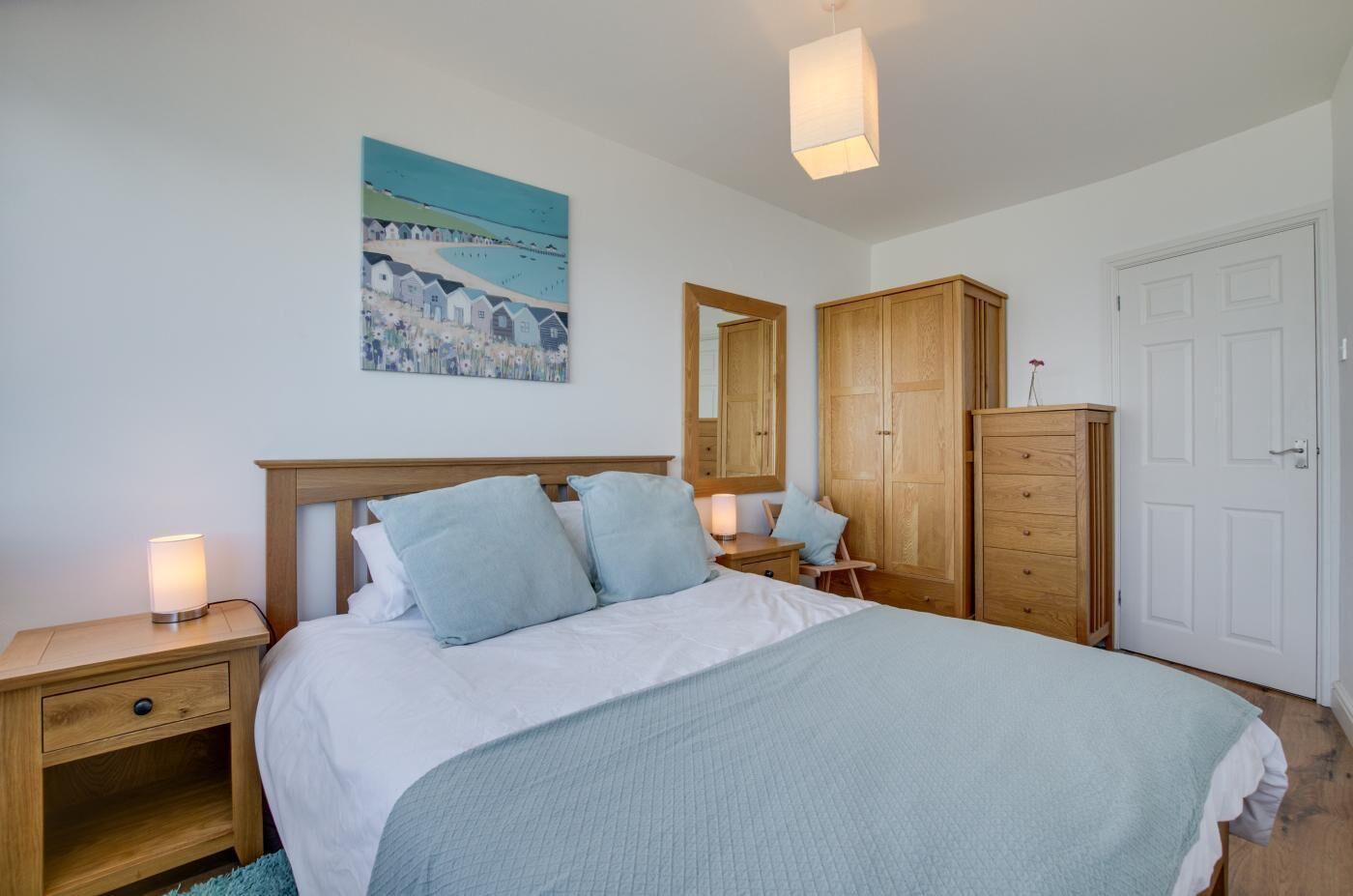 A bedroom with a bed, bedside tables, a dresser, a mirror, and a painting on the wall.