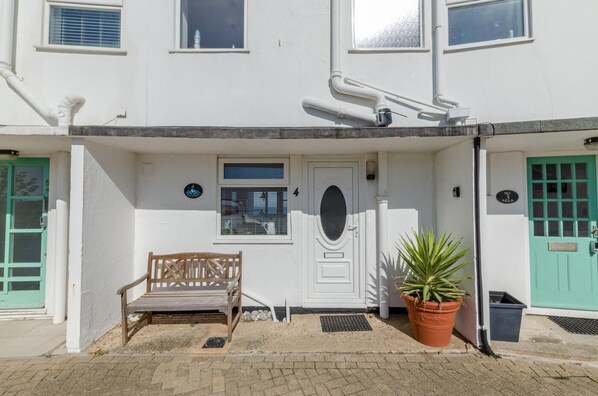 A white building with a green door, a bench, and a potted plant in front. - 5 Bed in Sheringham (oc-1450) (Sheringham)