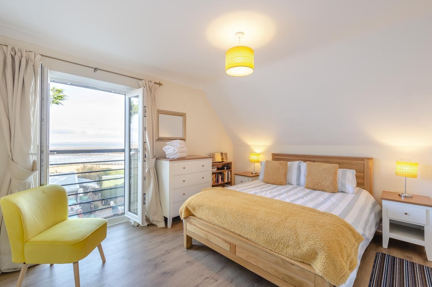 Une chambre avec un grand lit, une table de chevet, une commode, une chaise, une fenêtre avec des rideaux et une vue sur l’extérieur.