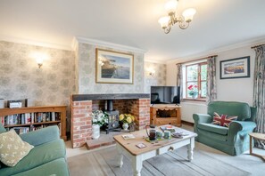 A cozy living room with a fireplace, a television, a bookshelf, and a green armchair. - 3 Bed in Weybourne (oc-716) (Weybourne)