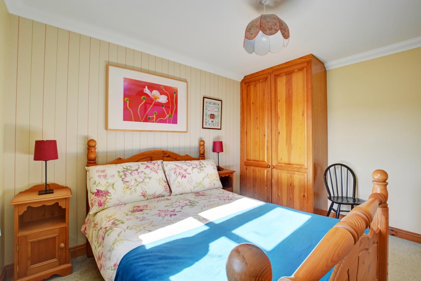 Een slaapkamer met een bed, een houten kledingkast, twee nachtkastjes, een stoel en een plafondventilator.