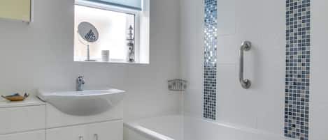 Une salle de bain moderne avec un lavabo blanc, des toilettes, une douche avec une porte en verre et une fenêtre avec un store bleu.