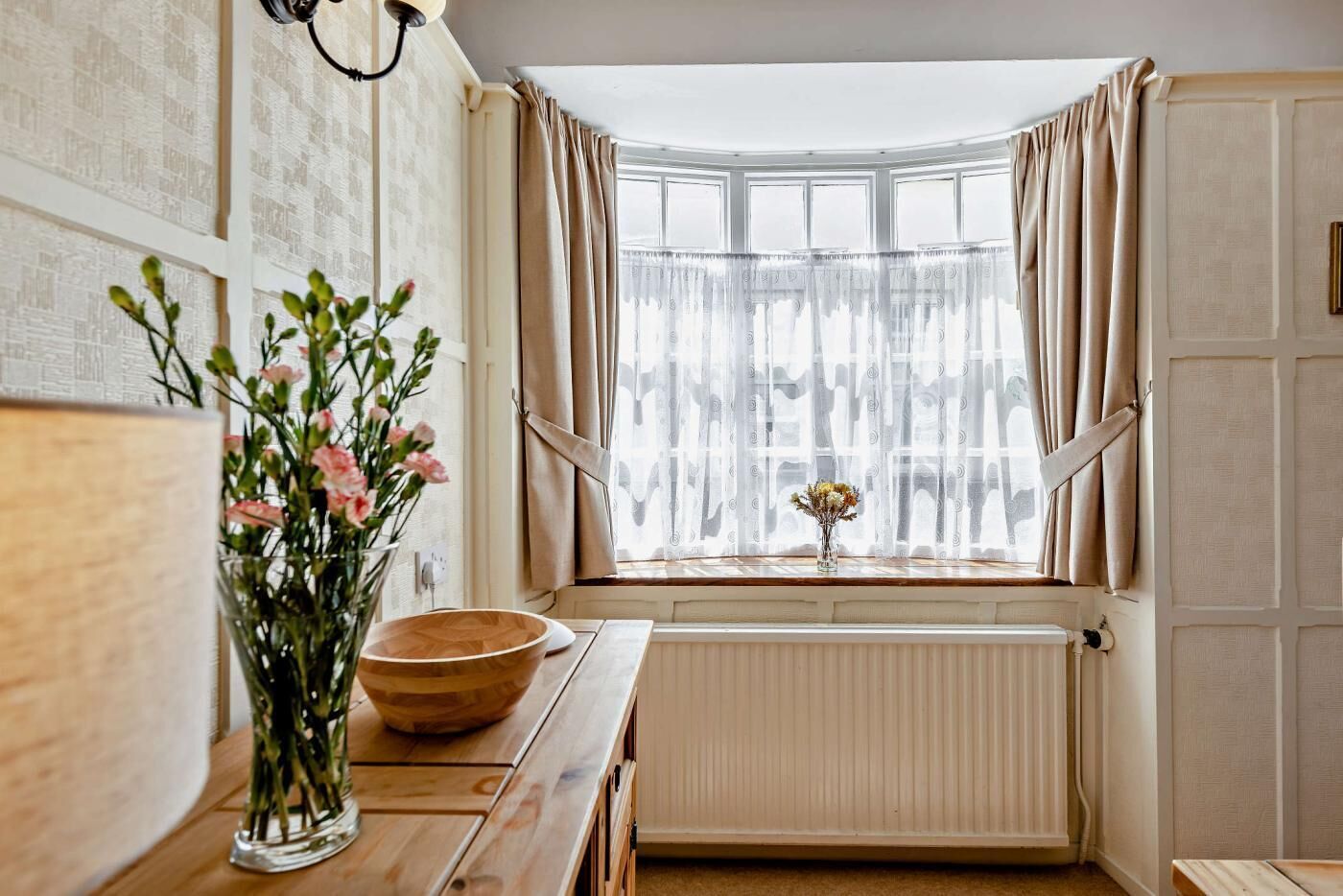 A kitchen with a wooden table, a vase with flowers, and a window with curtains.