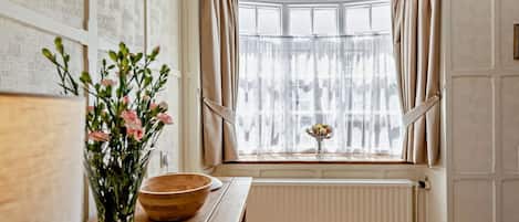 A kitchen with a wooden table, a vase with flowers, and a window with curtains.
