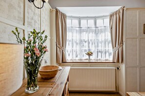 A kitchen with a wooden table, a vase with flowers, and a window with curtains. - 2 Bed in Ilfracombe (oc-quay) (Ilfracombe)