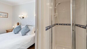 Habitación de hotel con cama, mesita de noche, lámpara de pared y zona de ducha con paredes de azulejos.