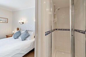 A hotel room with a bed, a nightstand, a wall-mounted light fixture, and a shower area with tiled walls. - 2 Bed in Ilfracombe (oc-quay) (Ilfracombe)