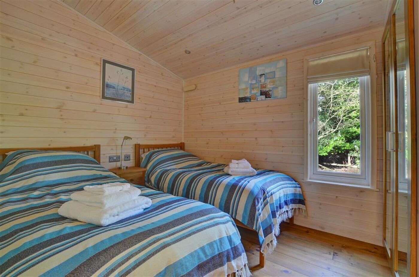 Una cabana amb dos llits, una finestra que dona als arbres i un quadre a la paret.