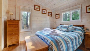 Ein Schlafzimmer einer Holzhütte mit einem Bett, einem Schminktisch, einer Bank und gerahmten Bildern an der Wand.