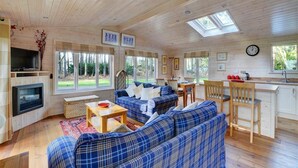 Ein gemütliches Blockhausschlafzimmer mit Holzbalkendecke, einem Wohnbereich mit blau kariertem Sofa, einem Kamin und einer Küche mit Holzbalken.