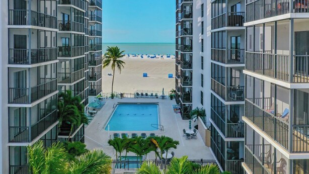 Um hotel moderno com piscina, várias varandas e vista para a praia.