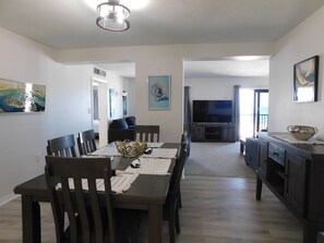 A dining area with a dark wooden table and chairs, a TV in the background, and artwork on the walls. - Island Winds Direct Gulf Front 2/2 condo on Fort Myers Beach (Fort Myers Beach)
