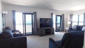 Uma sala de estar ampla com televisão de tela plana, dois sofás, uma mesa de centro e uma varanda com vista para o mar.