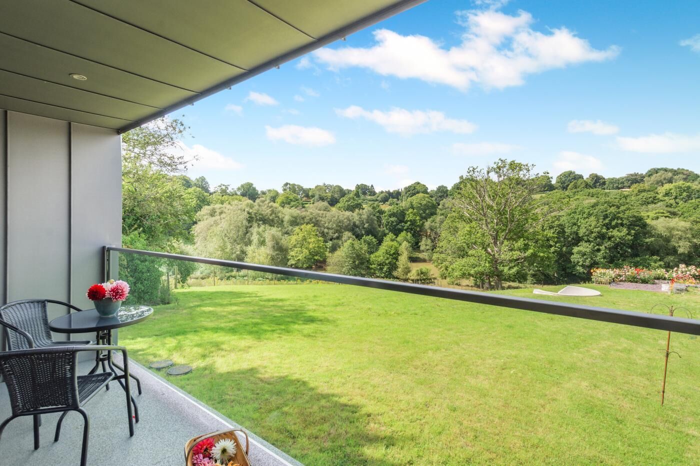 A balcony with a table and chairs, overlooking a grassy area and trees.