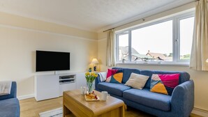 Een moderne woonkamer met een blauwe bank, een houten salontafel en een flatscreen televisie.
