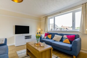 Ein modernes Wohnzimmer mit einem blauen Sofa, einem Holztisch und einem Flachbildfernseher.