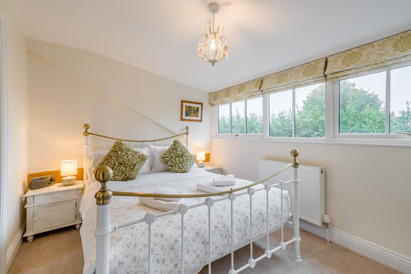 Une chambre à coucher avec un lit à baldaquin, un radiateur, une table de chevet avec une lampe et une fenêtre donnant sur un paysage verdoyant.