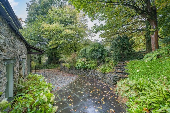 Een stenen pad dat leidt naar een traditioneel stenen gebouw met een groene deur, omringd door weelderige begroeiing en bomen.