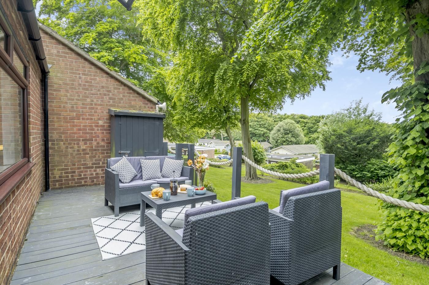 Un patio al aire libre con mobiliario de mimbre, una mesa con un florero y vista a una zona residencial.
