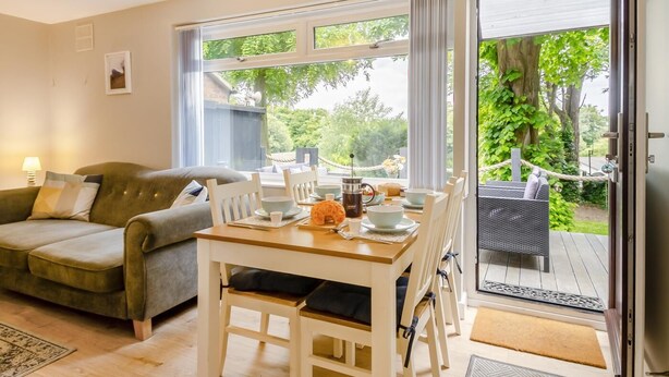 Una sala de estar acogedora con sofá, mesa de comedor, sillas y vista al jardín a través de amplios ventanales.