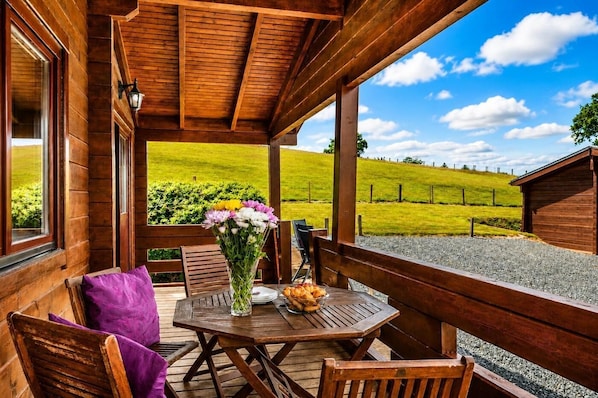 A wooden deck with a table and chairs, a vase of flowers, and a view of a green field.
