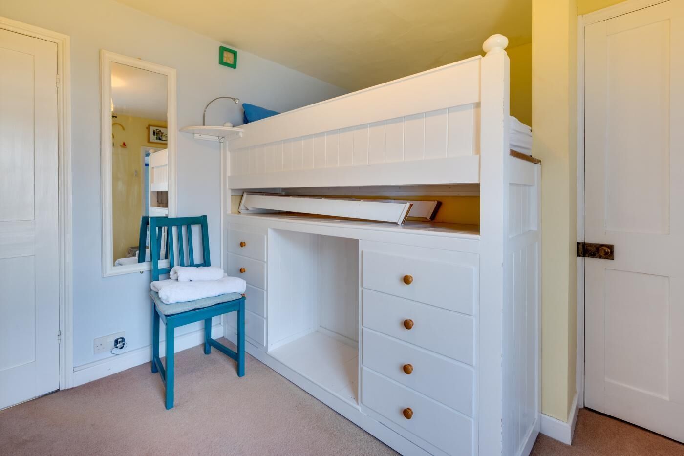 A room with a bunk bed, a chair, a mirror, and a dresser with drawers.