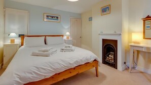 Ein Schlafzimmer mit einem hölzernen Bett, weißer Bettwäsche, zwei Nachttischlampen, einem Kamin und einem kleinen Tisch mit einer Lampe.