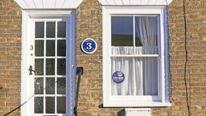 Ein Backsteinhaus mit weißer Tür und Fenster, beschriftet mit der Nummer 3 und einem Schild mit der Aufschrift 'Stay Here'.