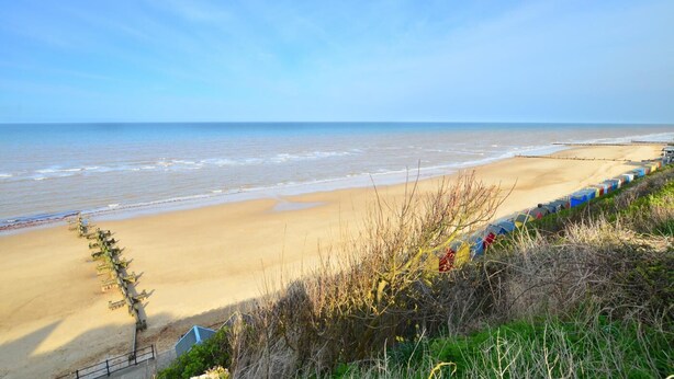 Une plage avec un rivage sablonneux, une rangée de cabanes de plage aux couleurs vives et un ciel bleu dégagé.