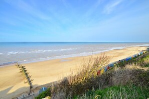 Ein Strand mit sandigem Ufer, eine Reihe bunter Strandhütten und ein klarer, blauer Himmel.