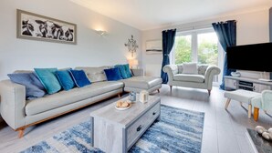 Un salon moderne avec un canapé gris, des coussins bleus, une table basse et un téléviseur.
