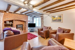 A cozy living room with leather sofas, a fireplace, a flat-screen TV, and a painting on the wall.