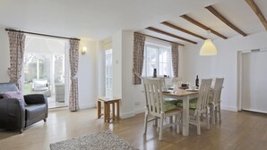 Un salon spacieux comprenant un coin repas, avec un canapé, une table dressée pour quatre personnes et une grande fenêtre agrémentée de rideaux.