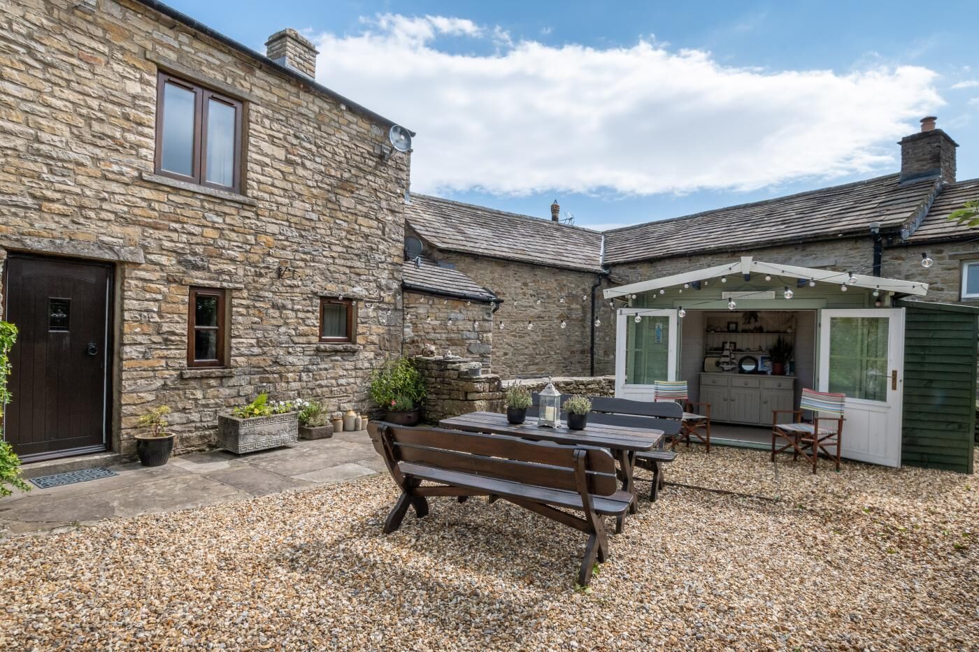 A stone house with a gravel patio, a wooden bench, and a small garden area.