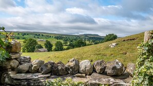 A stone wall with a rural landscape in the background, including rolling hills and scattered trees. - 3 Bed in Carperby (oc-ds1033) (Carperby)