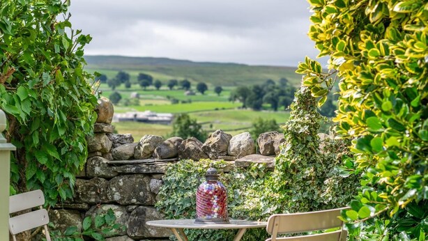 A stone wall with ivy, a table with a glass jar, and a view of a green valley. - 3 Bed in Carperby (oc-ds1033) (Carperby)