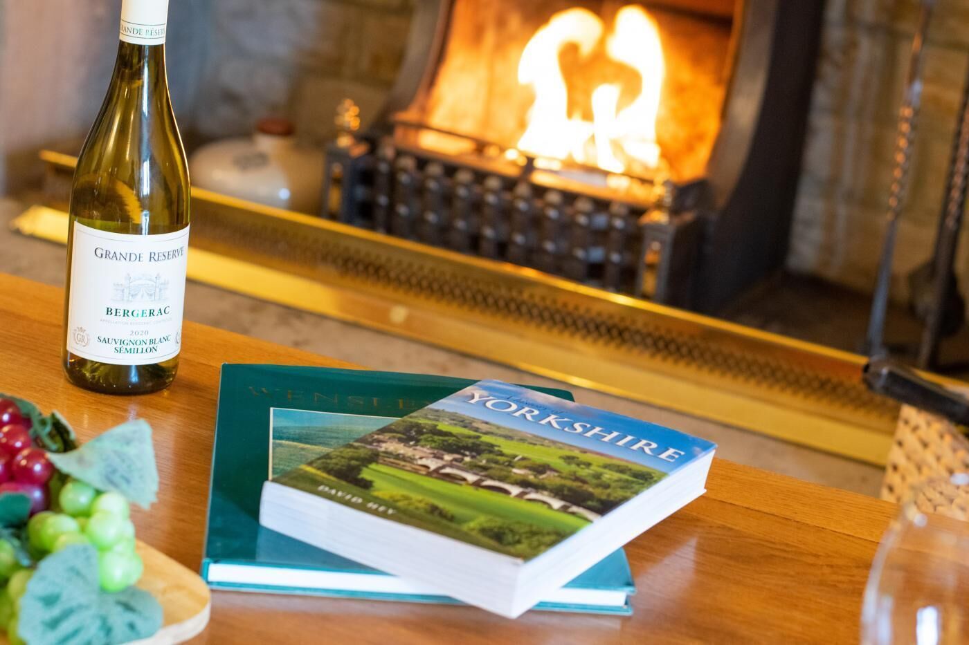Une bouteille de vin, un livre intitulé « Yorkshire », et quelques raisins sur une table en bois.