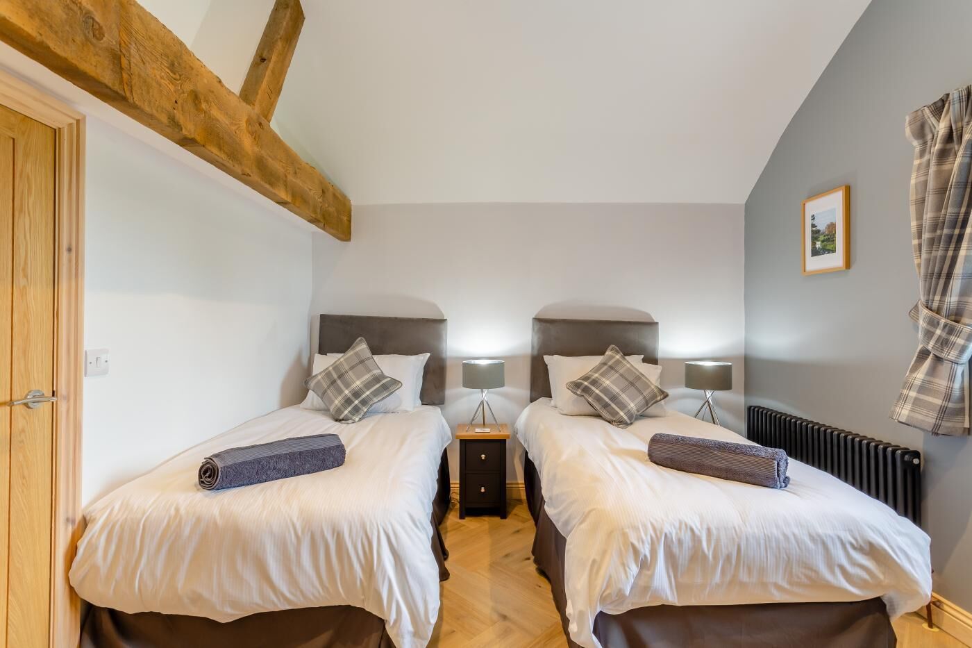A twin room with two beds, a wooden ceiling beam, a radiator, and a framed picture on the wall.