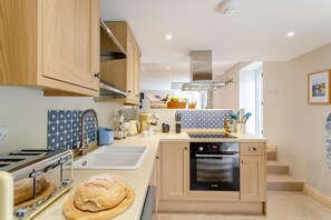 A modern kitchen with wooden cabinets, a built-in oven, and a countertop with various appliances and utensils. - 2 Bed in Summerbridge (oc-o32940) (Hartwith cum Winsley)