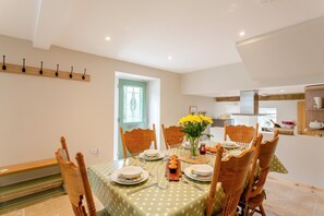 A dining area with a table set for four, chairs, a vase with flowers, and a kitchen in the background. - 2 Bed in Summerbridge (oc-o32940) (Hartwith cum Winsley)