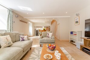 Ein modernes Wohnzimmer mit Sofa, Sesseln, Couchtisch und Fernseher.