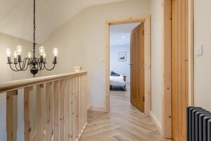 Un couloir avec une rambarde en bois, un lustre et un lit en arrière-plan.
