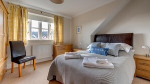 A bedroom with a bed, a chair, a nightstand, a lamp, and a window with curtains.
