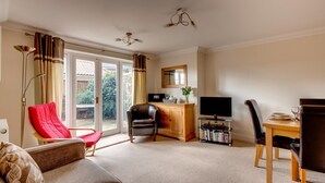 A living room with a sofa, red chair, TV, wooden cabinet, and a dining table with chairs.